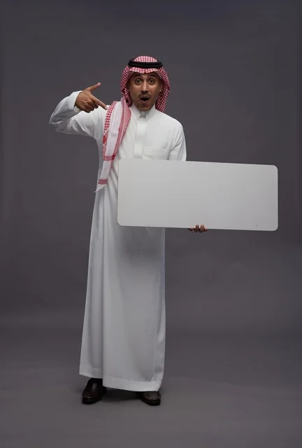 رجل سعودي يحمل لوحة بيضاء فارغة بتعبير مندهش