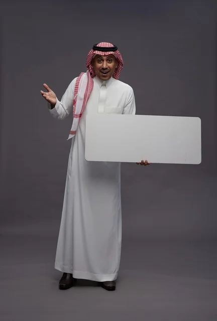 رجل سعودي يحمل لوحة إعلانية بيضاء فارغة في استوديو