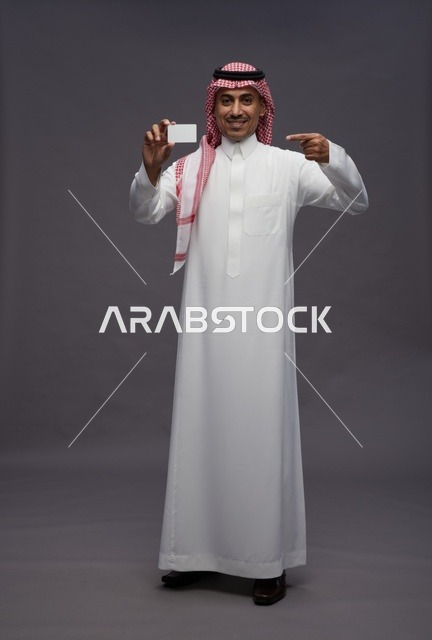 رجل سعودي بالزي التقليدي يحمل بطاقة ائتمان بيضاء