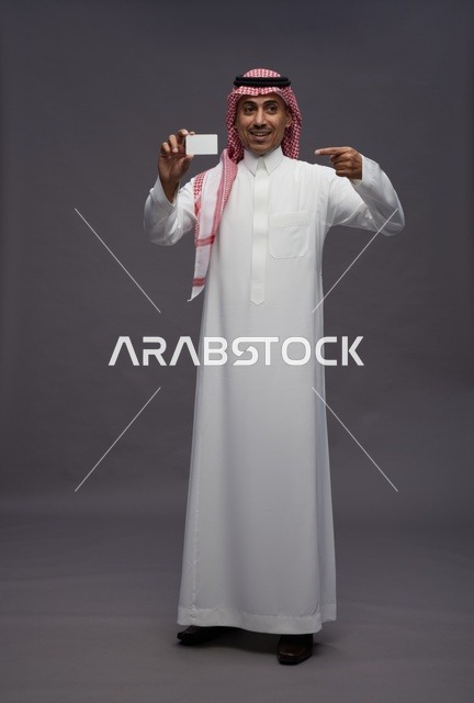 رجل سعودي بالزي التقليدي يحمل بطاقة ائتمان بيضاء