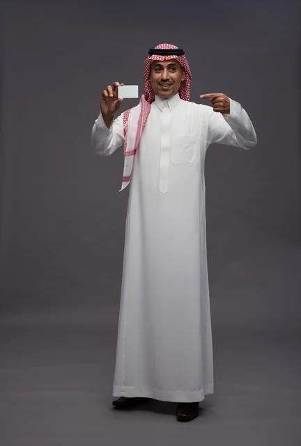 رجل سعودي بالزي التقليدي يحمل بطاقة ائتمان بيضاء