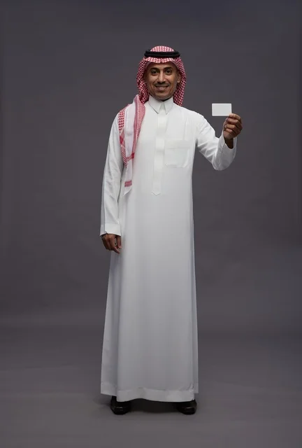 رجل سعودي بالزي التقليدي يحمل بطاقة ائتمان بيضاء