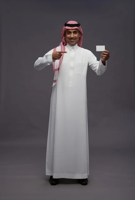 رجل سعودي بالزي التقليدي يحمل بطاقة ائتمانية بيضاء