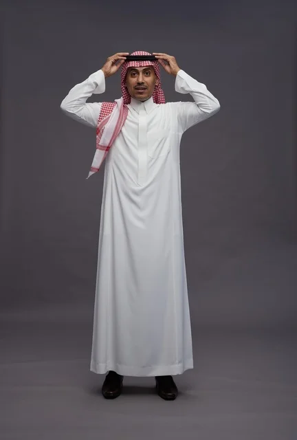 رجل سعودي مندهش يرتدي الزي التقليدي في استوديو رمادي