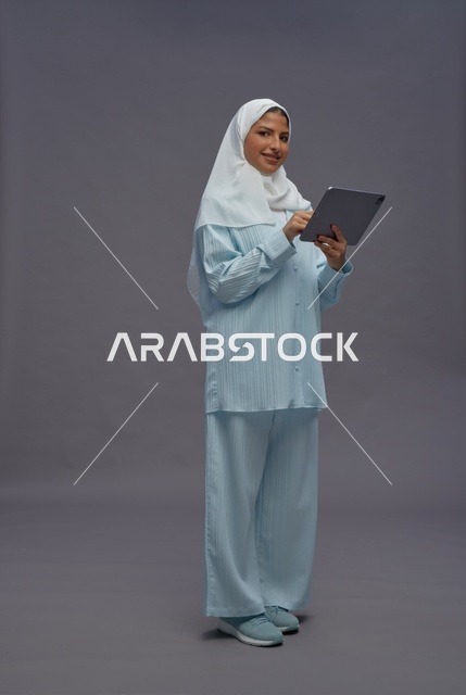 امرأة سعودية بزي محتشم تستخدم جهازاً لوحياً