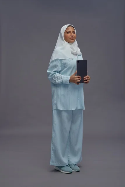 امرأة سعودية بزي كاجوال محتشم تحمل جهازاً لوحياً