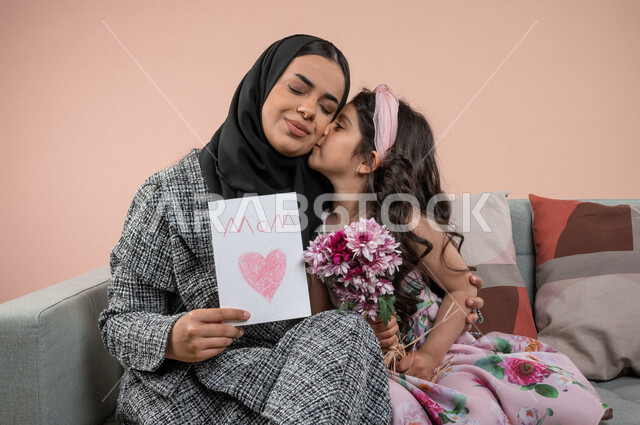 بورتريه لطفلة عربية خليجية سعودية تقبل امها ، تقدم الورود الجميلة وبطاقة المعايدة لوالدتها بايماءات تدل على الفرح والسعادة ، هدية يوم الأم ، عيد أم سعيد ،  عيد ميلاد ، اعياد ومناسبات سعيدة 