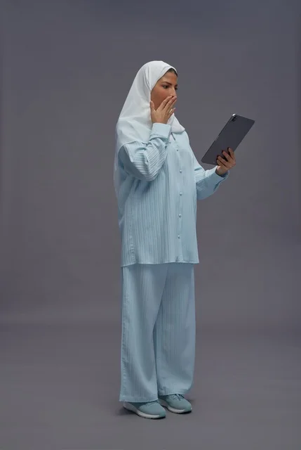 امرأة سعودية متفاجئة تستخدم جهازاً لوحياً بخلفية رمادية