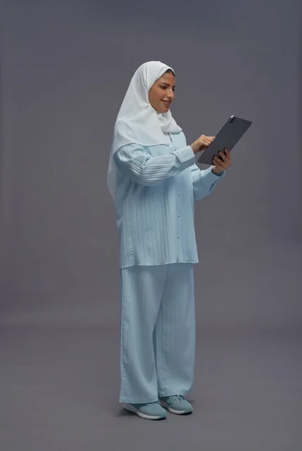 امرأة سعودية تستخدم جهازاً لوحياً بزي كاجوال محتشم