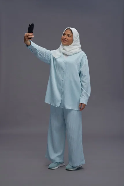 امرأة سعودية بملابس كاجوال تلتقط سيلفي في الاستوديو