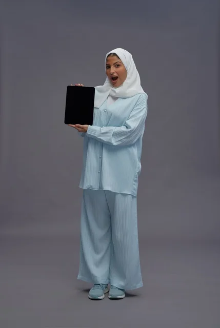 امرأة سعودية تحمل جهاز لوحي بتعبير وجه مندهش