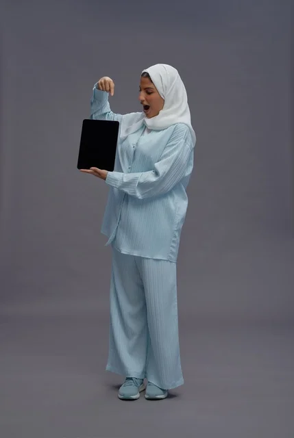 امرأة سعودية تمسك بجهاز لوحي بخلفية رمادية