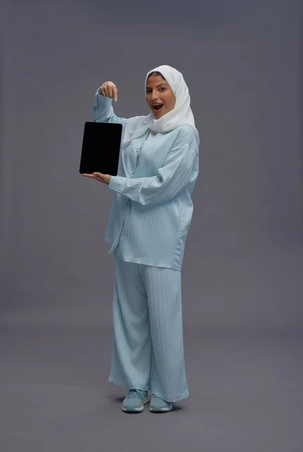 امرأة سعودية تمسك بجهاز لوحي بخلفية رمادية