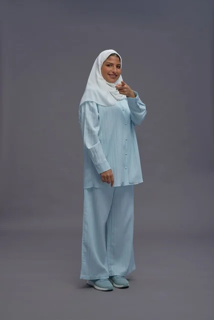 امرأة سعودية بزي كاجوال أزرق فاتح تشير نحو الكاميرا