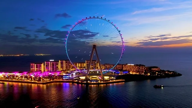 عين دبي مضاءة ليلاً في جزيرة بلوواترز مع انعكاس البحر