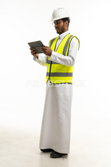 مهندس سعودي بالثوب وسترة السلامة يستخدم جهاز لوحي