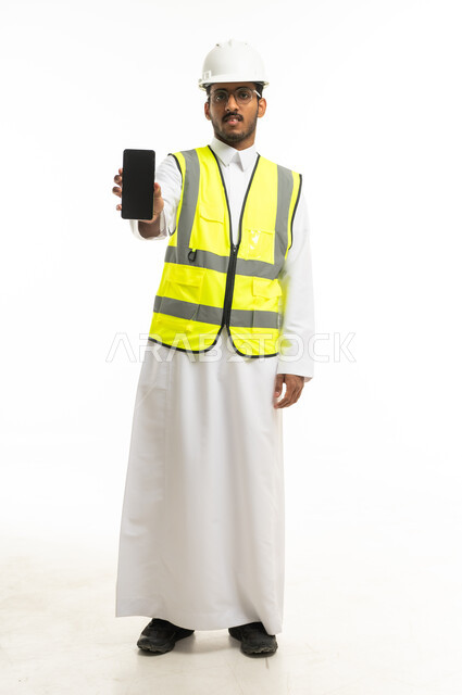 مهندس سعودي بمعدات السلامة يحمل هاتفاً ذكياً