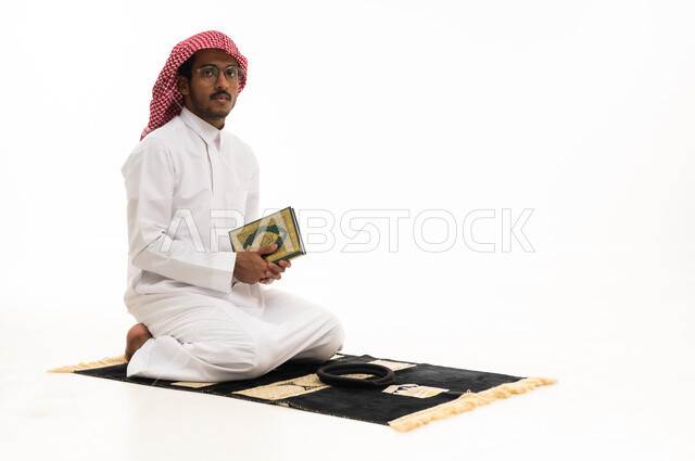 رجل سعودي يمسك بالمصحف الشريف على سجادة الصلاة