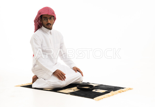 رجل سعودي يصلي على سجادة بخلفية بيضاء