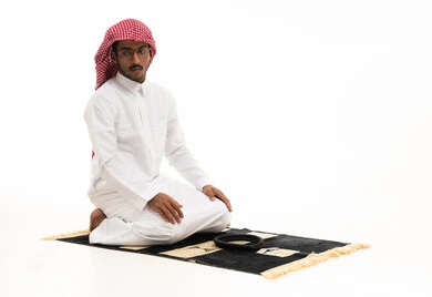 رجل سعودي يصلي على سجادة بخلفية بيضاء