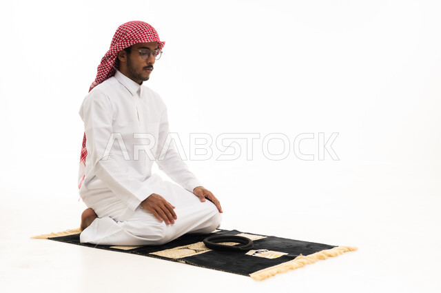 رجل سعودي يصلي على سجادة الصلاة خلفية بيضاء