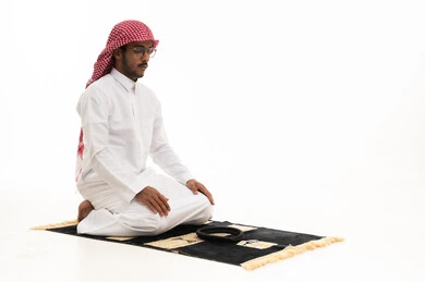 رجل سعودي يصلي على سجادة الصلاة خلفية بيضاء