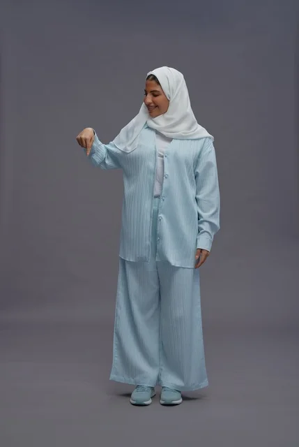 امرأة سعودية بالحجاب تشير للأسفل في استوديو رمادي