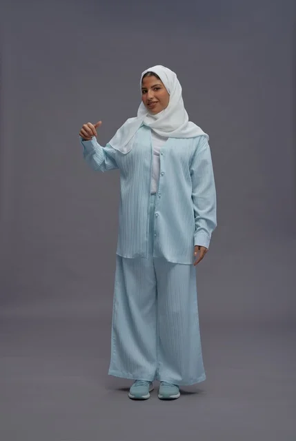 امرأة سعودية بالحجاب ترفع إبهامها أمام خلفية رمادية