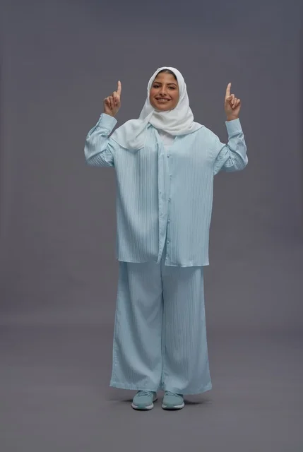 امرأة سعودية تشير للأعلى أمام خلفية رمادية