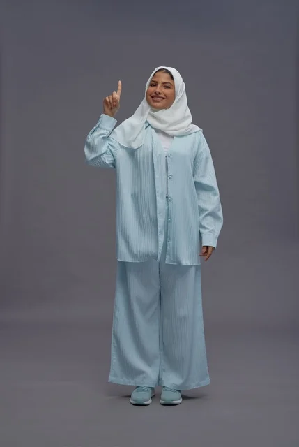 امرأة سعودية بالحجاب تشير للأعلى خلفية رمادية