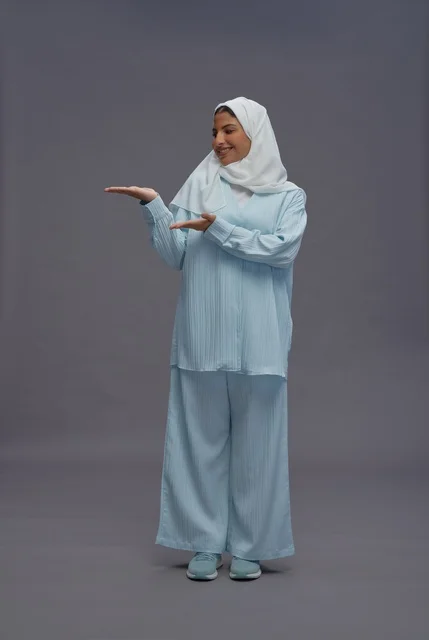 امرأة سعودية بالحجاب تشير للجانب على خلفية رمادية