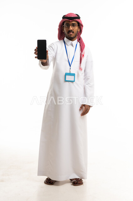 رجل أعمال سعودي يحمل هاتفاً ذكياً بخلفية بيضاء