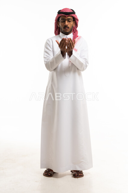 رجل سعودي بالثوب التقليدي يدعو أمام خلفية بيضاء