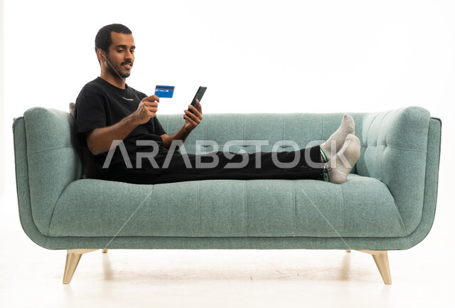 رجل عربي يستخدم بطاقة ائتمان وهاتف على الأريكة