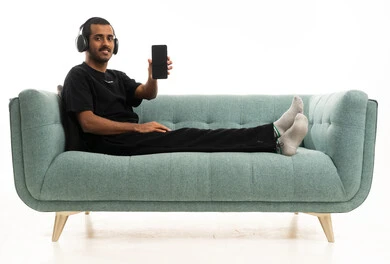 شاب سعودي على الأريكة يمسك هاتفاً ذكياً وسماعات