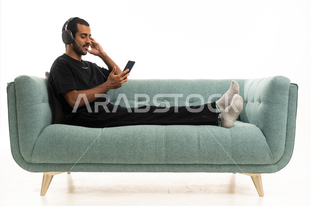 شاب سعودي مع سماعات يسترخي على أريكة في الاستوديو