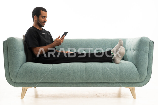 رجل عربي سعودي  يستخدم الحاسوب المحمول على الأريكة