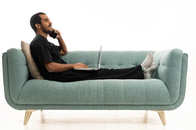 موظف عربي خليجي يستخدم الحاسوب المحمول على الأريكة