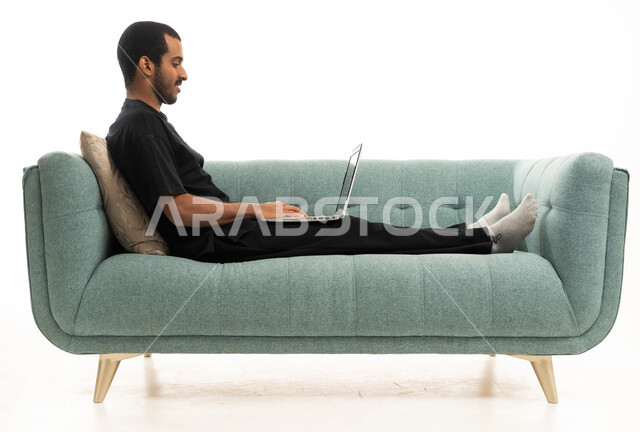 رجل سعودي يستخدم اللابتوب على أريكة خضراء حديثة