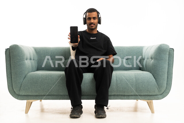 Saudi Man with Headphones and Smartphone on Sofa