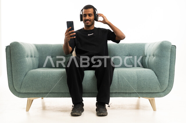Saudi Man Using Smartphone with Headphones on Sofa