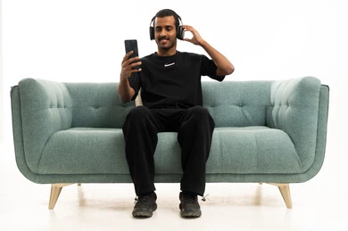 شاب سعودي يستخدم الهاتف الذكي والسماعات على أريكة