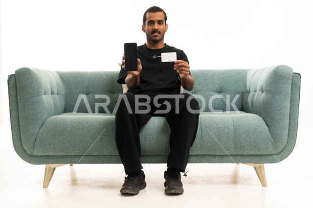 Arab Man Holding Smartphone and Blank Card on Sofa