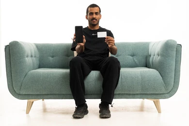 Arab Man Holding Smartphone and Blank Card on Sofa