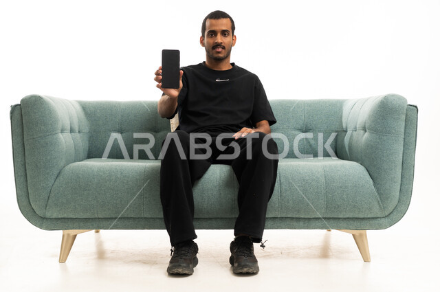 شاب عربي يمسك هاتف ذكي على أريكة حديثة