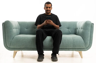 شاب سعودي يجلس على أريكة يستخدم الهاتف الذكي
