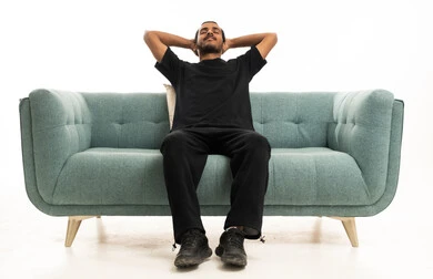 شاب سعودي يسترخي على أريكة خضراء بخلفية بيضاء