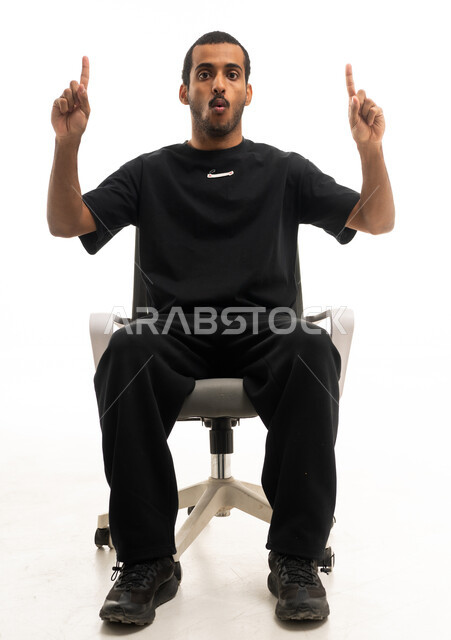 شاب سعودي يجلس ويشير للأعلى بتعبير متفاجئ