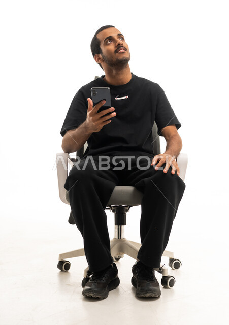 شاب سعودي جالس على كرسي يحمل هاتف ذكي