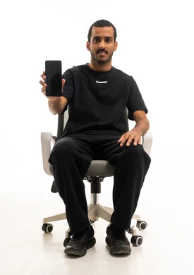 شاب عربي يجلس على كرسي يحمل هاتفا ذكيا